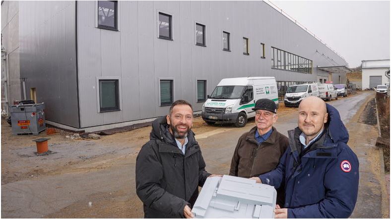 Drei Männer halten ein Produkt der Firma AKF Fahrzeugteile Bautzen in den Händen und lächeln in die Kamera.