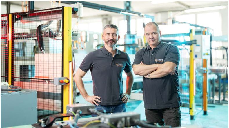 Matti Reppe und Holger Orawetz, Chefs und Inhaber der Qpoint Composite GmbH in Dresden stehen Seite an Seite in lässigen Poloshirts vor ihren Produktionsanlagen.