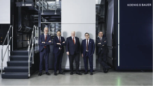 Fünf Männer stehen in blauen und schwarzen Anzügen in einer Herstellungshalle.