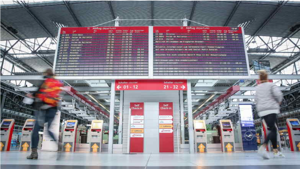 Eine große Anzeigetafel mit Abflügen und Anflügen. Darunter sind Check-In Schalter im Dresdner Flughafen.