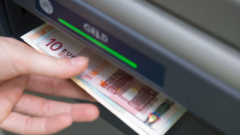 Eine Hand nimmt Geldscheine aus einem Geldautomaten.