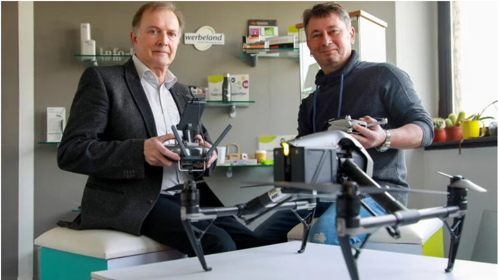 Zwei Männer sitzen im Büro und halten eine Drohne.