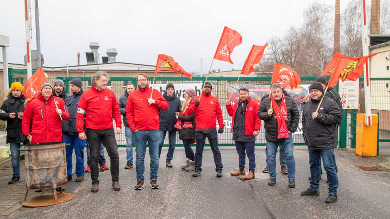 Mitarbeiter der IG Metall streiken vor den Toren der Firma mit Flaggen.