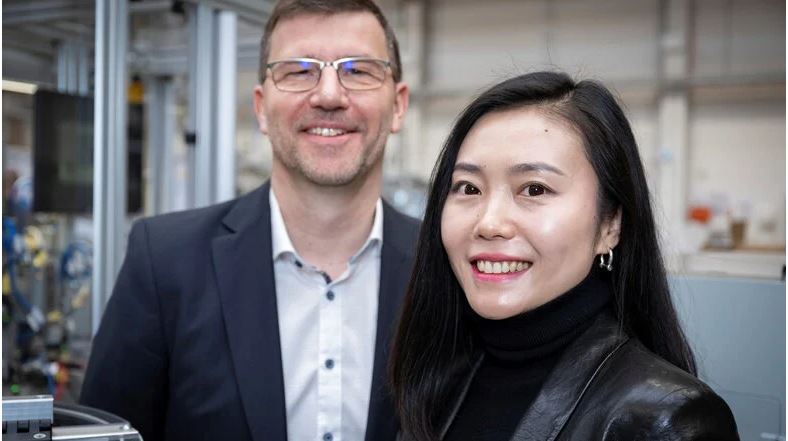 Die Geschäftsführerin des China-Geschäfts von Xenon Automatisierungstechnik steht im Vordergrund des Bildes und grinst in die Kamera. Im Hintergrund lacht Kay Truxa, der Geschäftsführer des Unternehmens in Dresden.