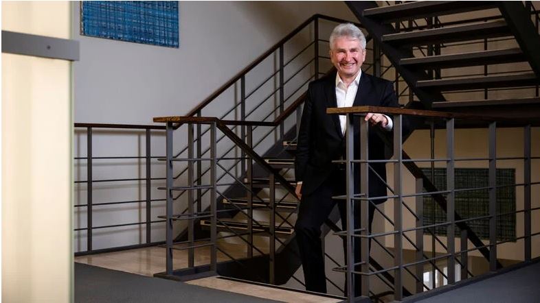 Prof. Dr. Andreas Pinkwart steht lachend in einem schwarzen Anzug im metallischem Treppenhaus eines Gebäudes der TU Dresden.