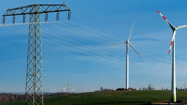 Ein Blick in eine Landschaft mit Strommasten und Windrädern. Der Himmel ist blau.