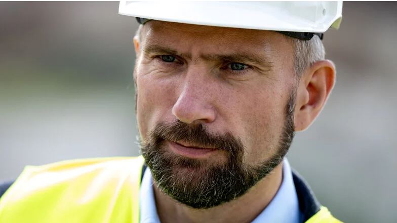 Martin Dulig (SPD) steht schaut mit ernstem Gesicht und Bauhelm in die Kamera. Er trägt eine Warnweste.