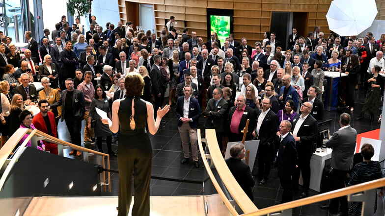 Das Foyer der Gläsernen Manufaktur ist gefüllt mit Unternehmer*innen. Eine Moderatorin steht auf einer Freitreppe und referiert.