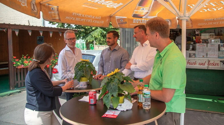 Mehrere Menschen stehen um einen Biertisch herum.