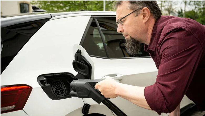 Ein Mann in bordeauxfarbenem Hemd lädt ein Elektroauto.