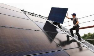 Das Bild zeigt einen Mann beim anbringen von Solarplatten auf einem Dach.
