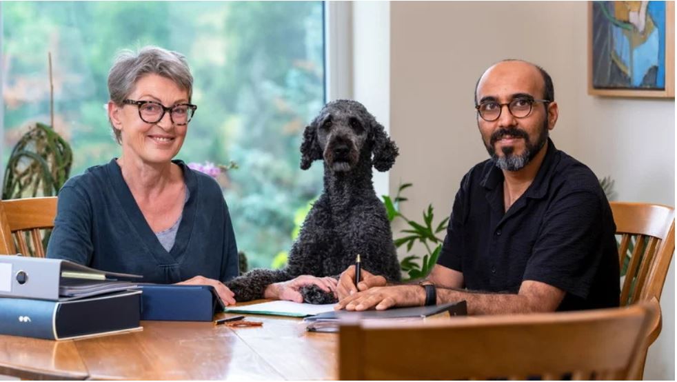 Man sieht eine Mann und ein Frau mit einem Hund an einem Tisch.