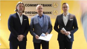 Man sieht drei Männer vor dem Commerz-Bank-Logo.