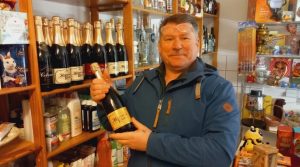 Man sieht Nikolai Jaworski, Besitzer von einem Laden mit russischen Spezialitäten. Er hält eine Weinflasche.