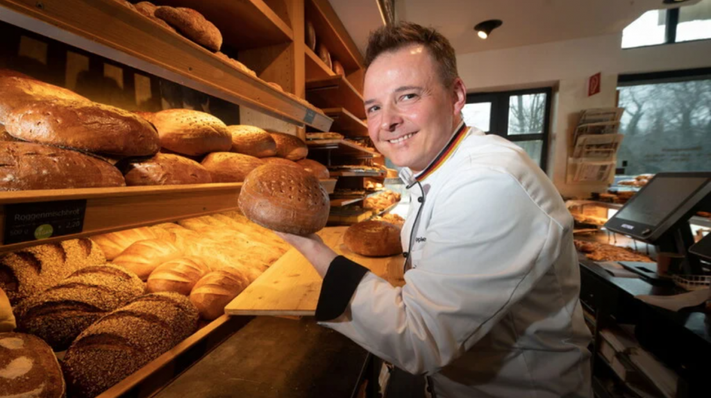 Man sieht einen Bäcker vor der Auslage.