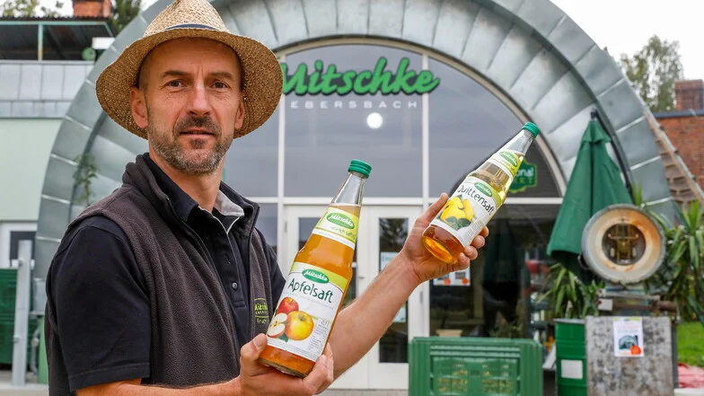 Mann hält zwei Glasflaschen gefüllt mit Apfelsaft und Juttensaft hoch.