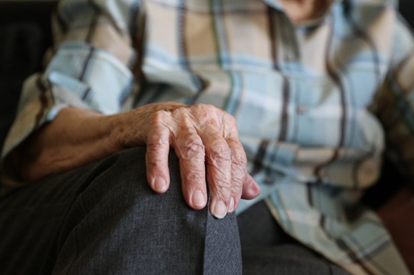 Eine ältere Person legt ihre Hand auf ein Knie.