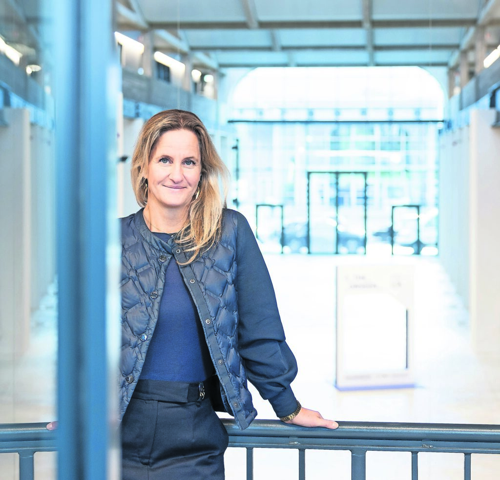 Eine Frau lehnt am Geländer in einer umgebauten Industriehalle und lächelt in die Kamera.