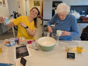 Eine Pflegedienstmitarbeiterin hilft einer Senioren bei Küchenarbeiten.