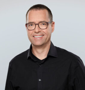 Ein Mann mit Brille lächelt in die Kamera.