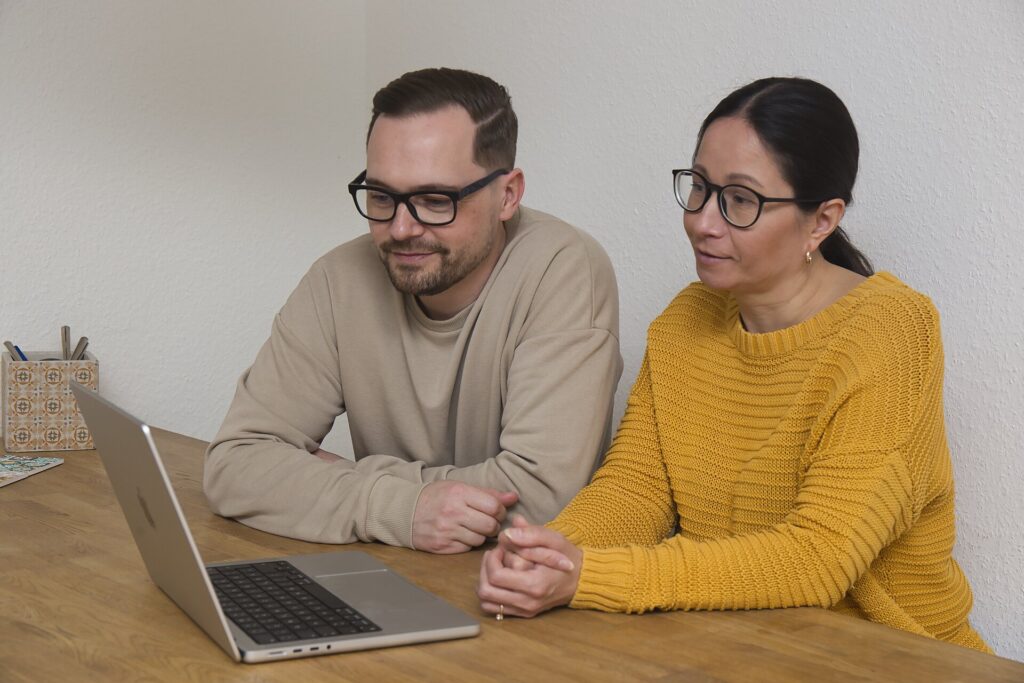 Zwei Menschen schauen auf einen Laptop-Bildschirm.