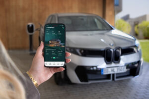 Eine Hand hält ein Handy, dahinter ist ein BMW zu sehen.